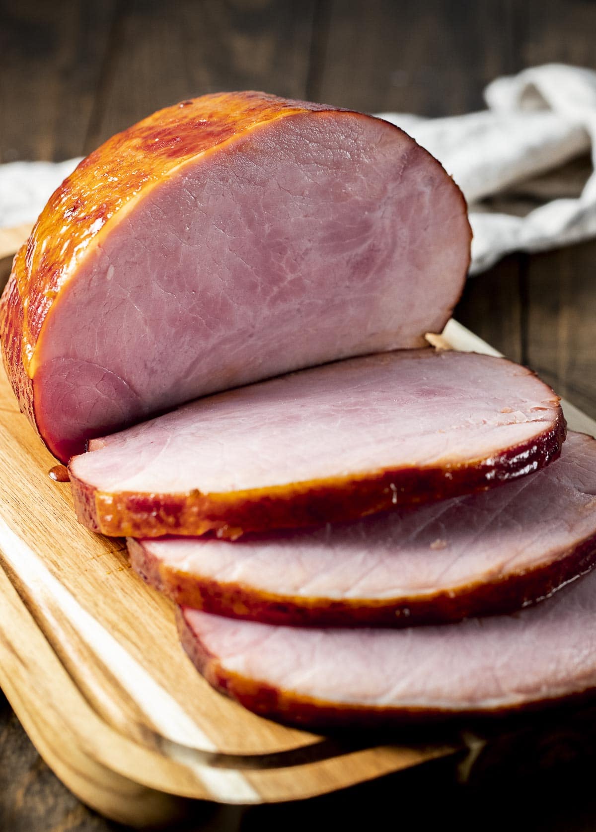 Side view of a boneless ham on a wooden board and cut into slices.