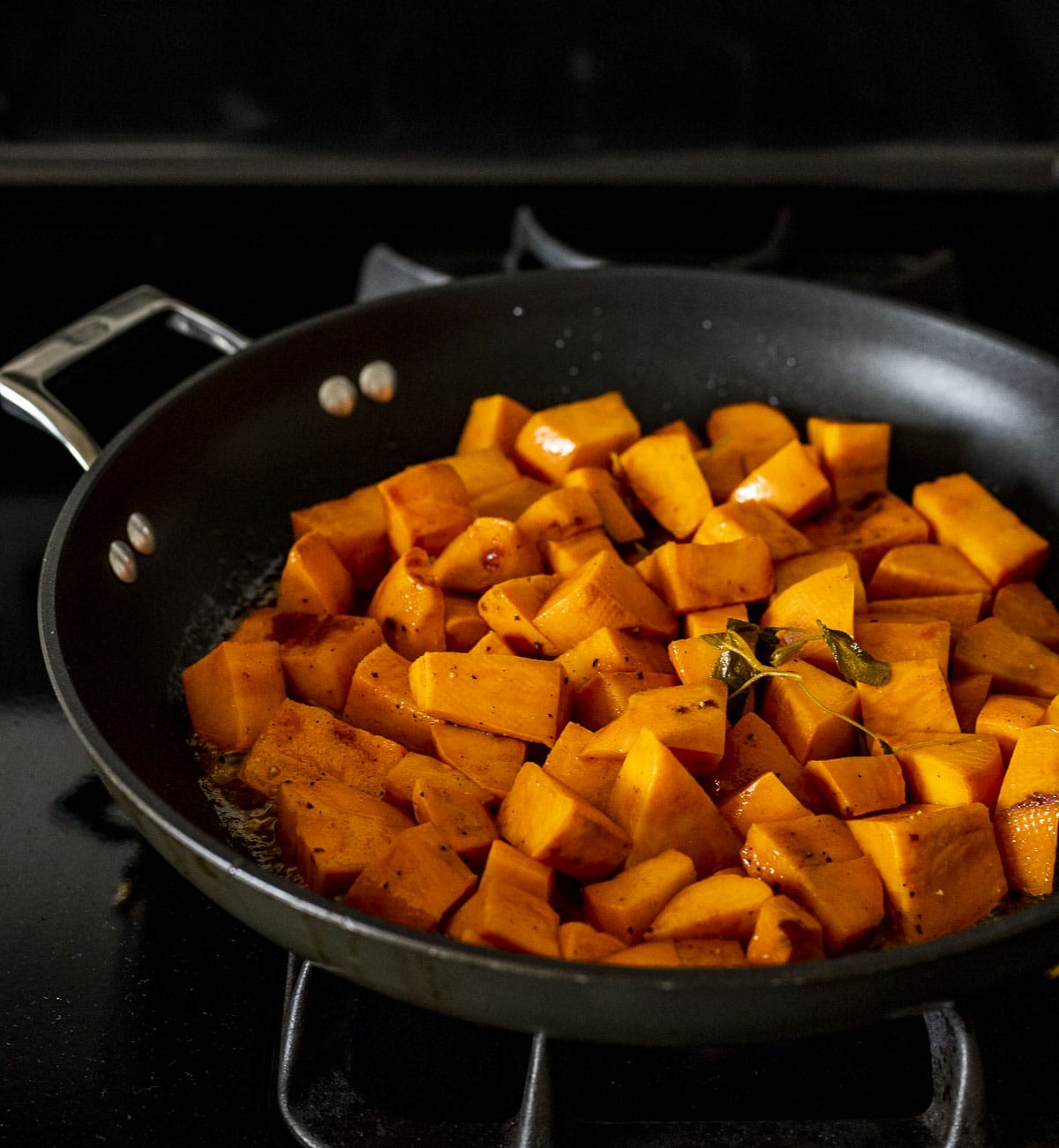 Sous vide sweet potato cubes being browned in a skillet on the stovetop.