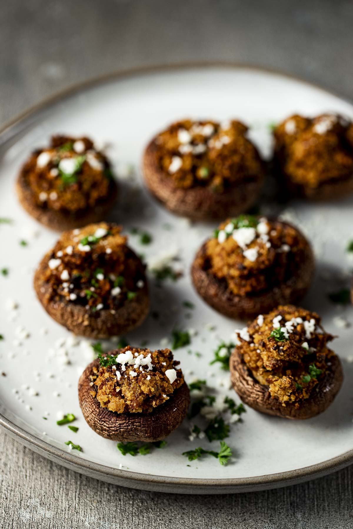 Stuffed mushrooms arranged on a white plate and topped with cilantro and cotija cheese.