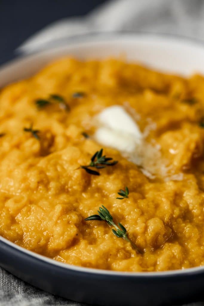 Close up side view of mashed sweet potatoes in a dish with butter on top.