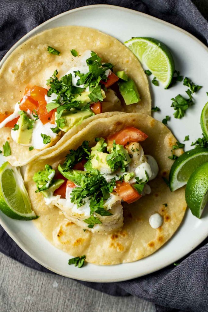 2 tacos on a plate garnished with cilantro, creamy white sauce and tomatoes