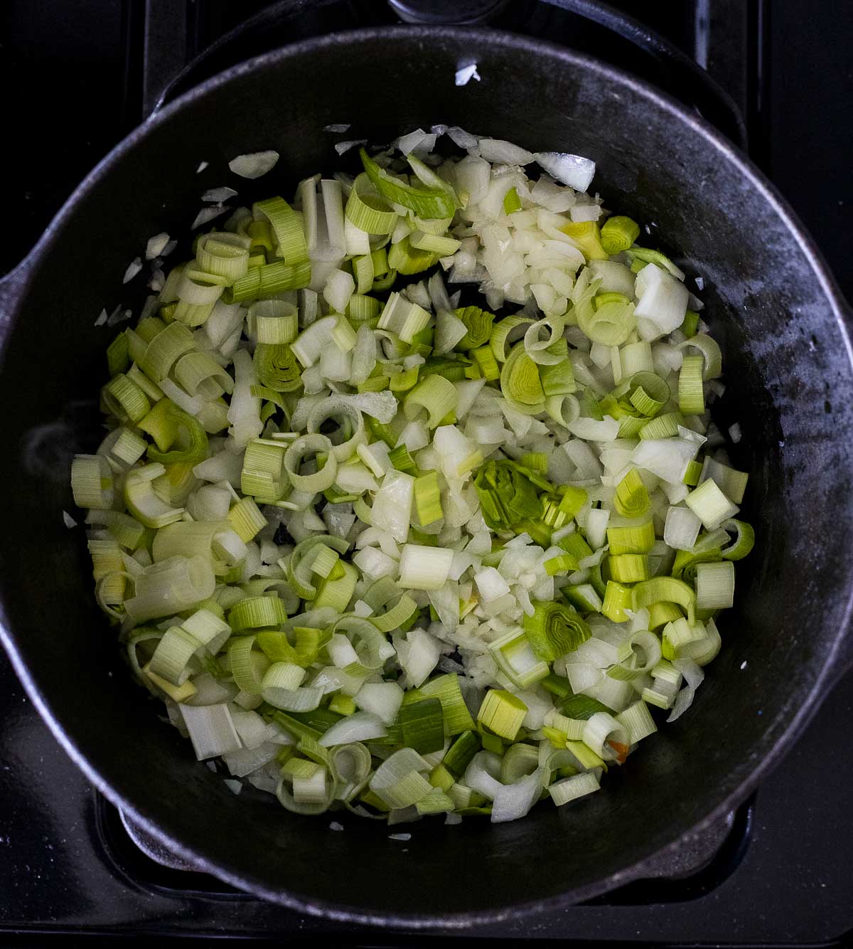Overhead view of garlic, onion and leeks sautéed in a large pot.