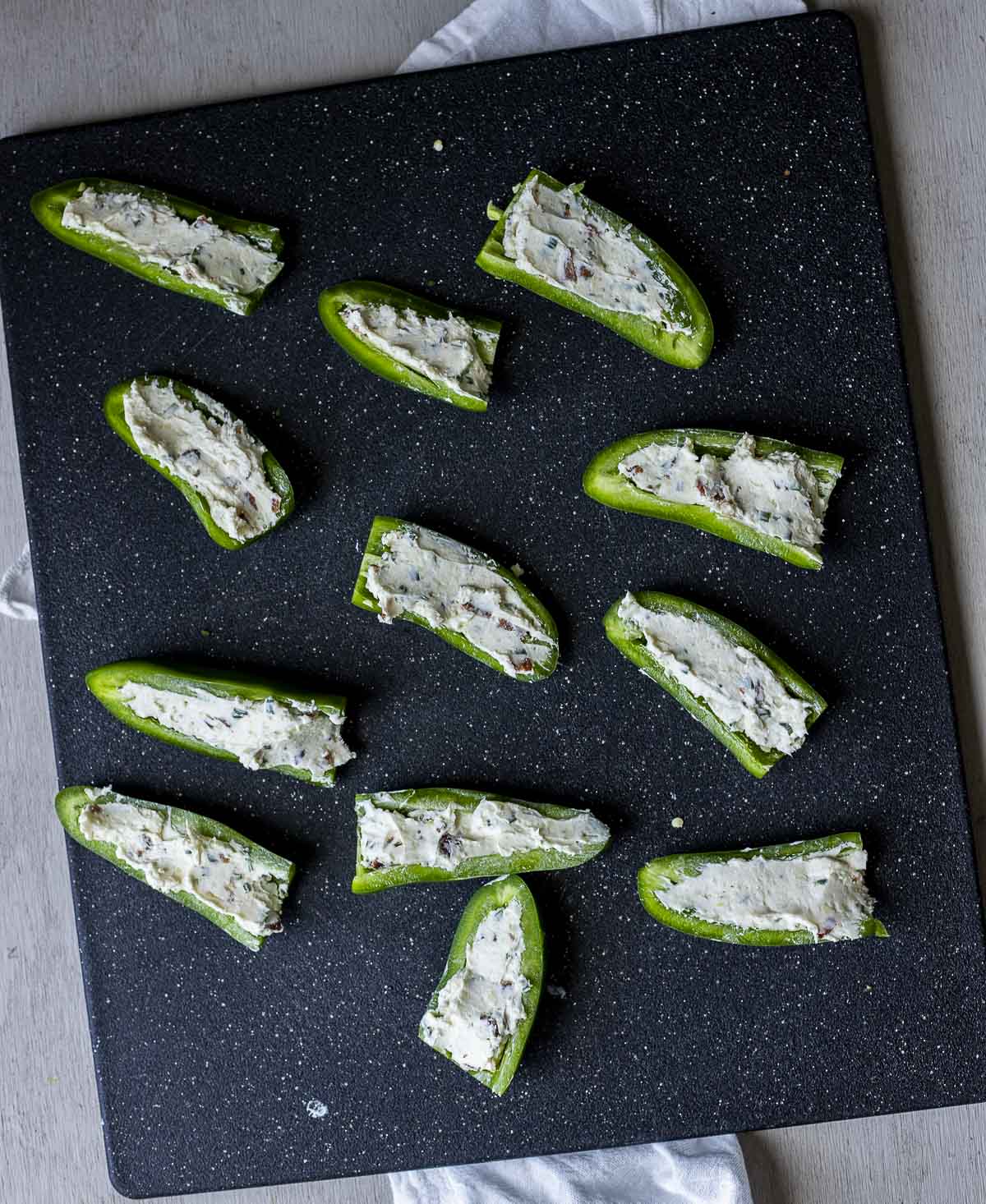Jalapeños arranged on a work surface and stuffed with cream cheese filling.