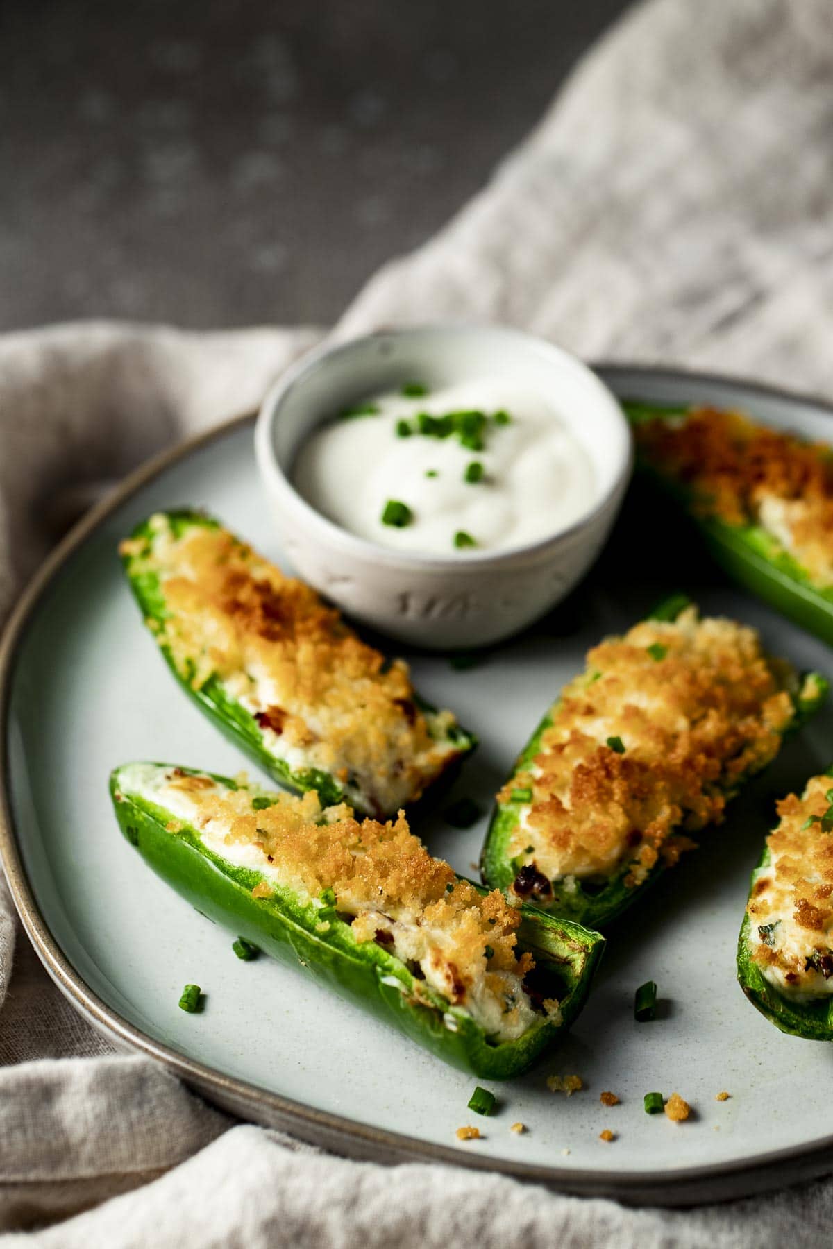Side view of jalapeno poppers on a plate with a small bowl of ranch dressing.