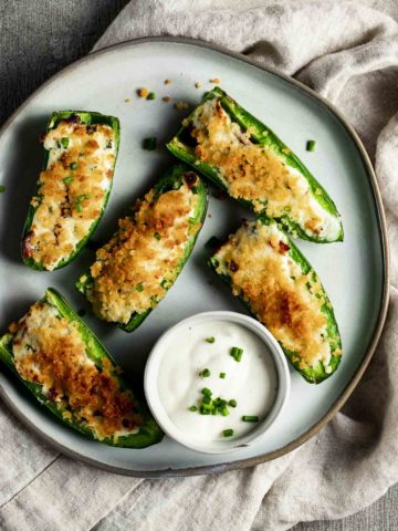 Overhead view of air fryer jalapeno poppers arranged on a plate with a small bowl of ranch dressing.