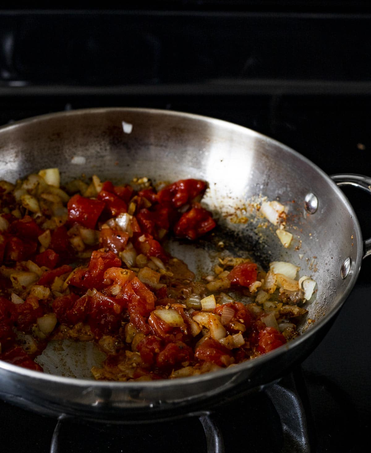 Tomatoes and aromatics being sautéed in a skillet.