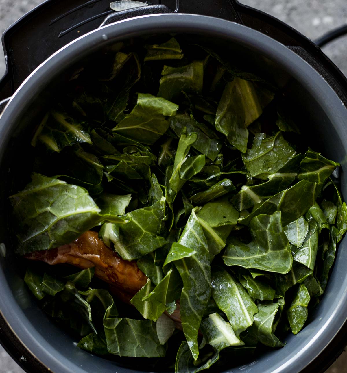 Chopped collard greens and smoked turkey wings in the Instant Pot insert.
