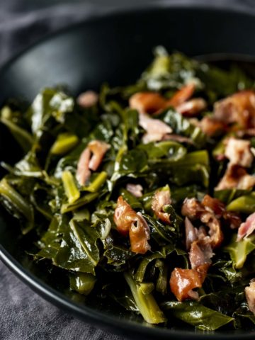 Side view of collard greens and smoked turkey in a black bowl.