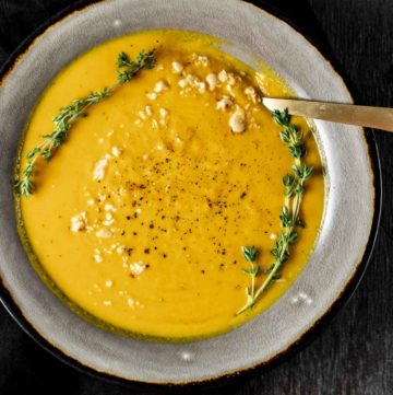 Overhead view of pumpkin soup in a grey bowl and garnished with sprigs of thyme and crushed hazelnuts.