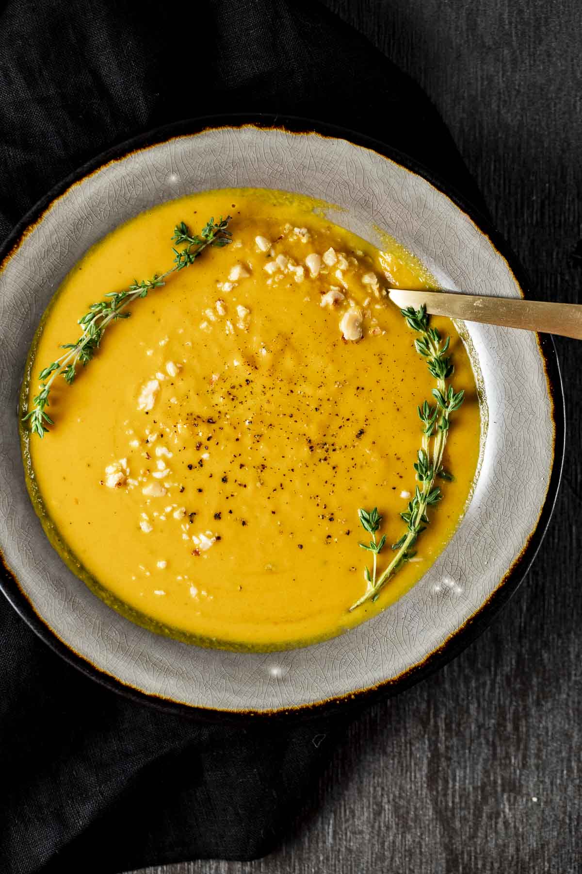 Overhead view of pumpkin soup in a grey bowl and garnished with sprigs of thyme and crushed hazelnuts.