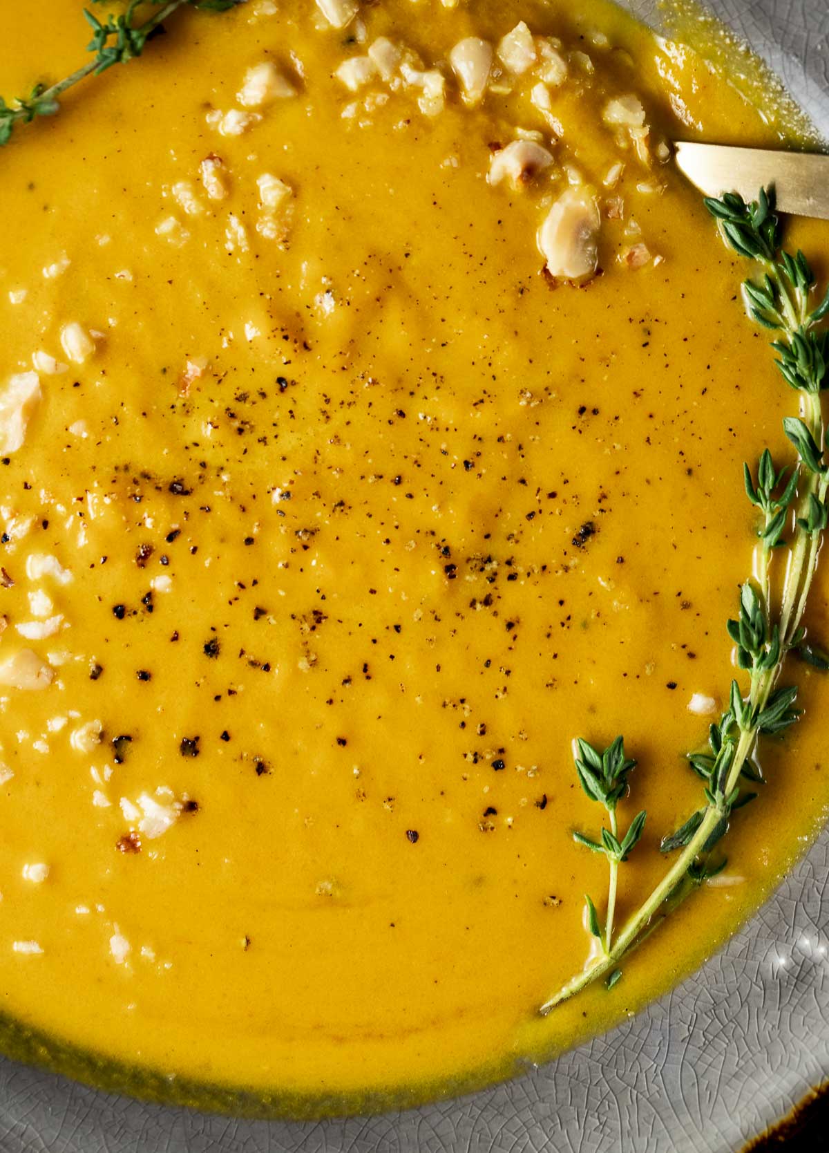 Up close view of pumpkin soup with fresh thyme and crushed hazelnuts on top.