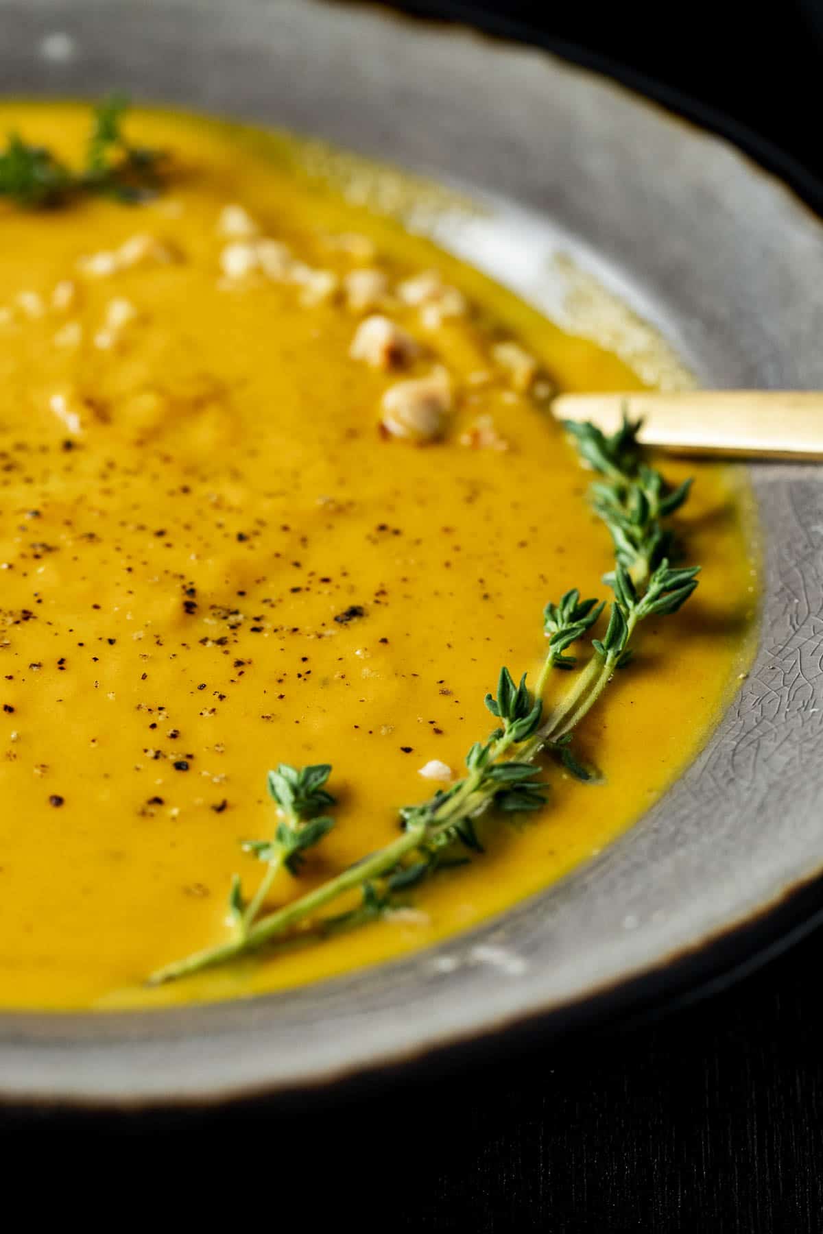Side view of pumpkin soup in a bowl with a sprig of fresh thyme on top.