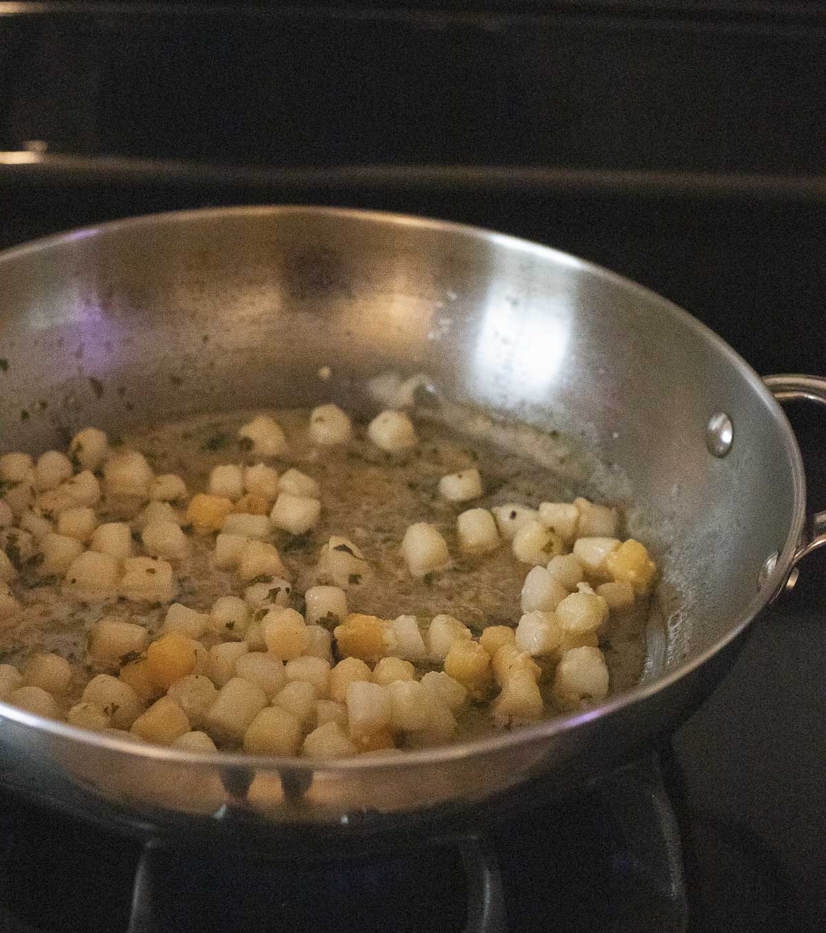 Scallops in scampi sauce in a skillet.