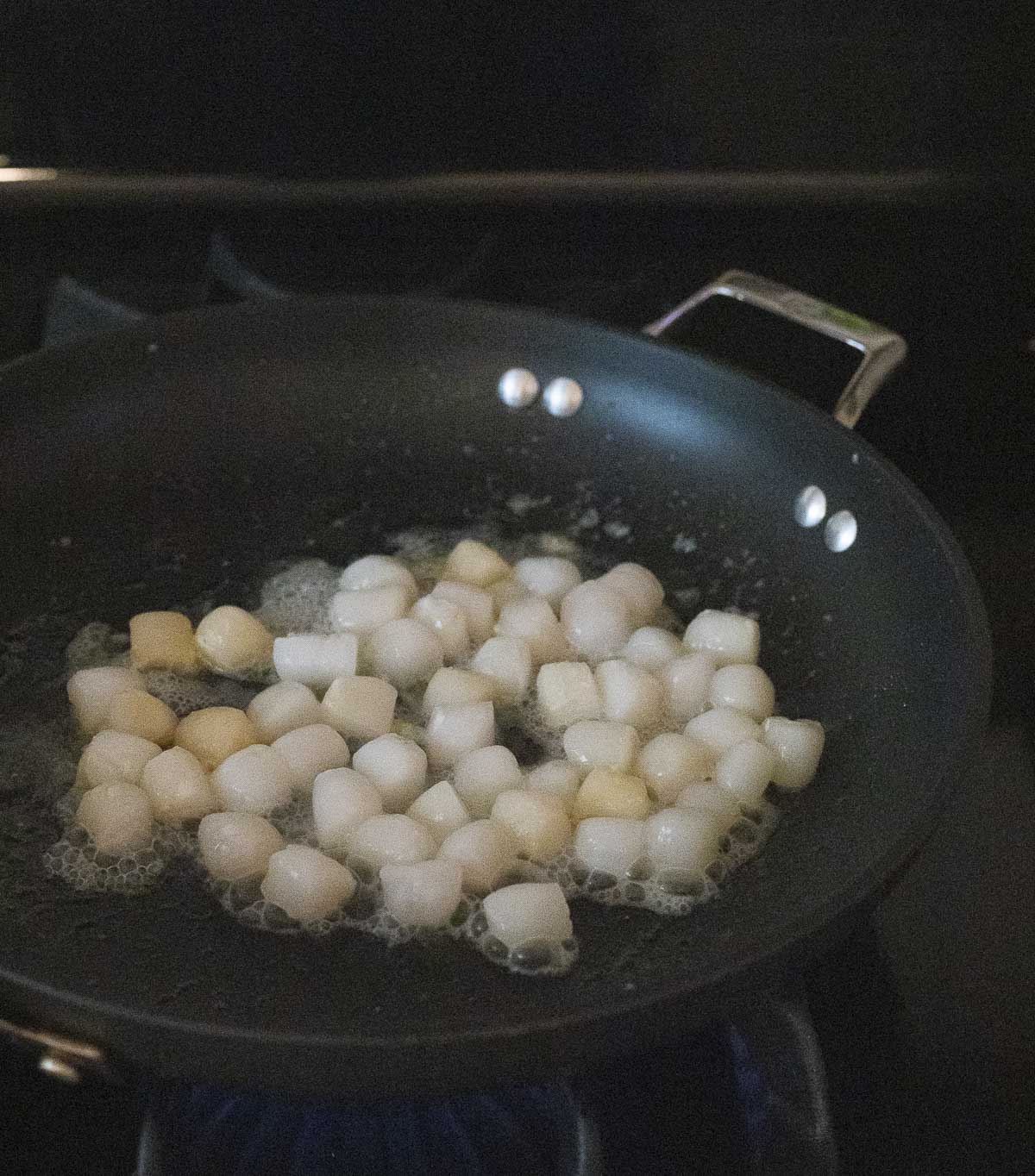 Bay scallops being seared with oil in a skillet.