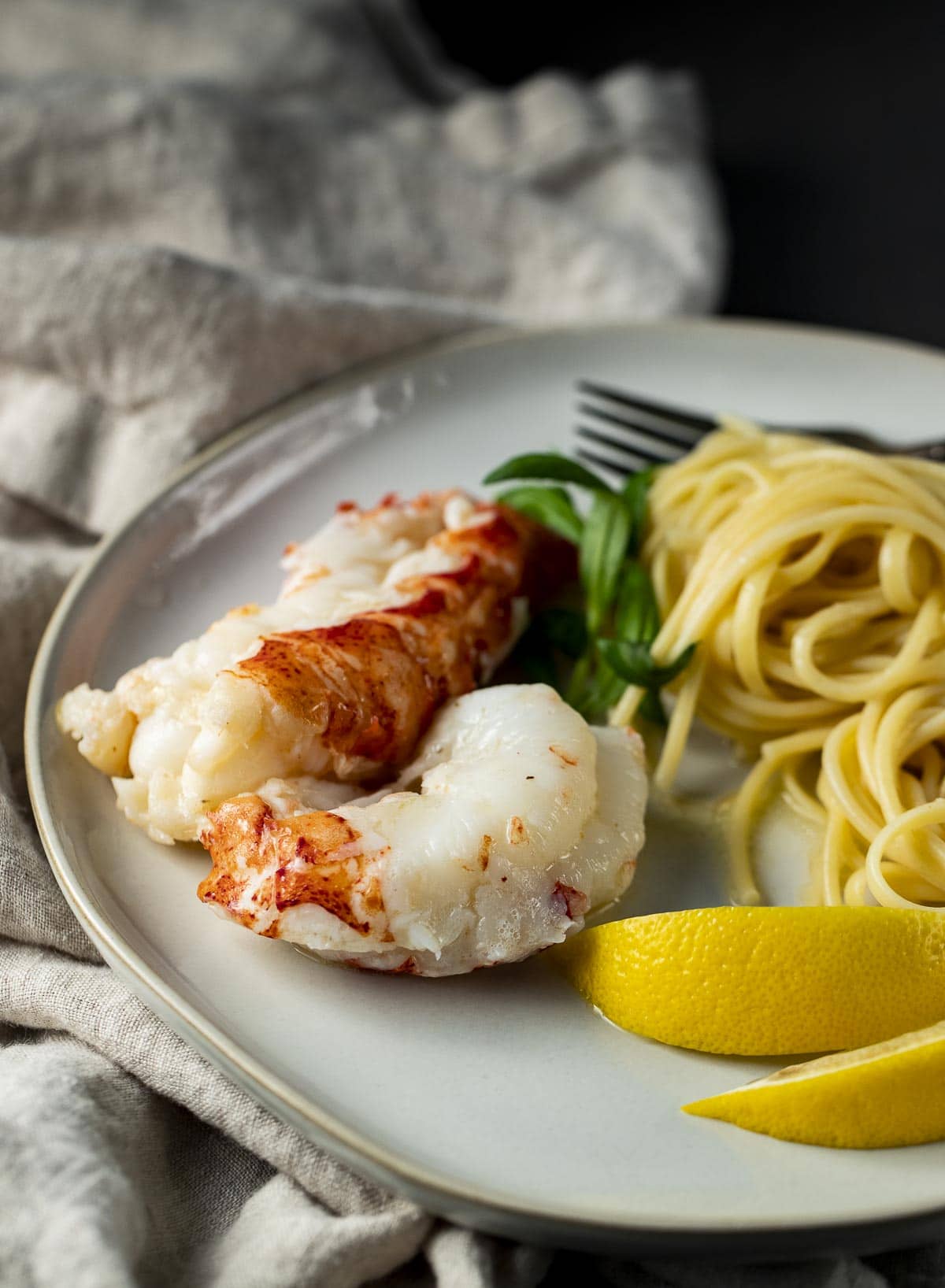 Lobster tails served with pasta and lemon wedges.