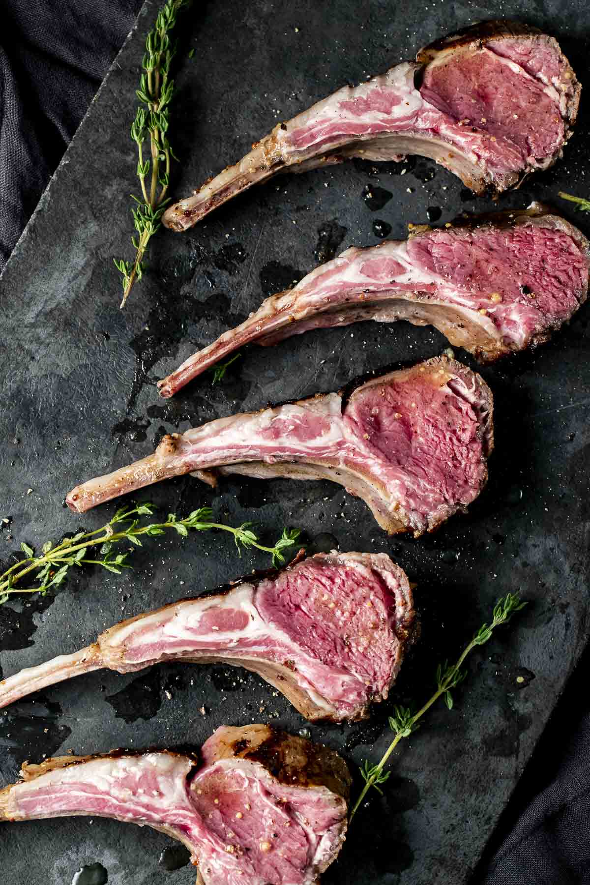 Overhead view of rack of lamb cut into chops and garnished with fresh herbs.