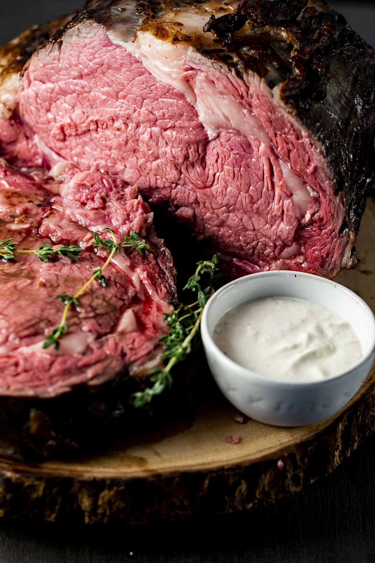 Rib roast on a wooden board with a small bowl of horseradish sauce on the side.