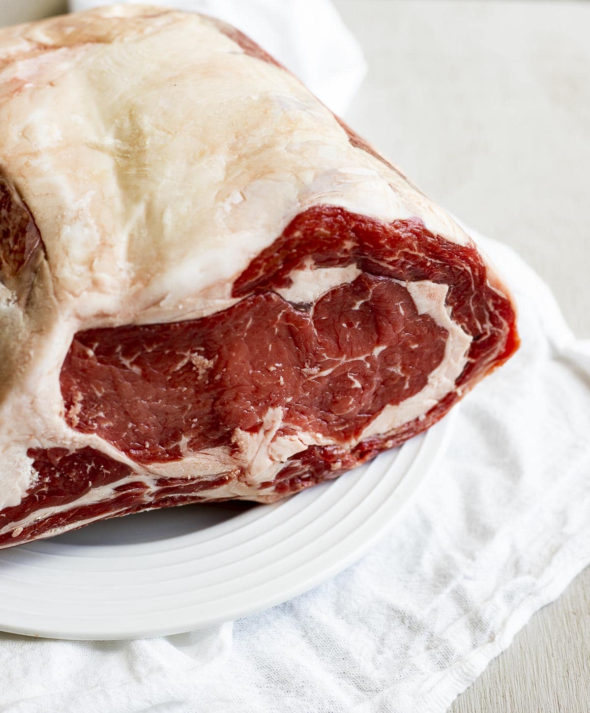 Side view of a raw prime rib roast on a white plate.