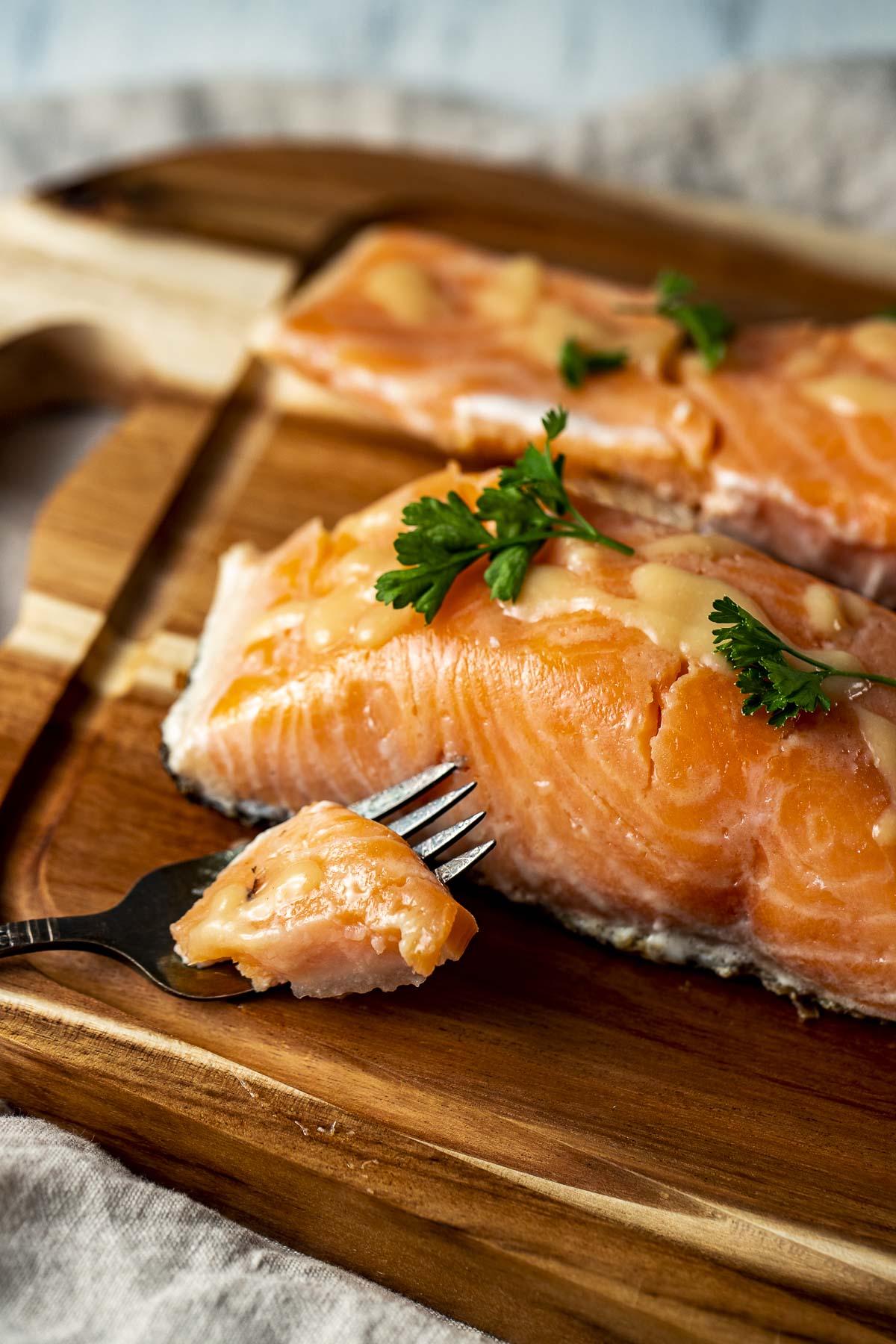 Side view of sous vide salmon on a wooden board with some salmon on a fork.
