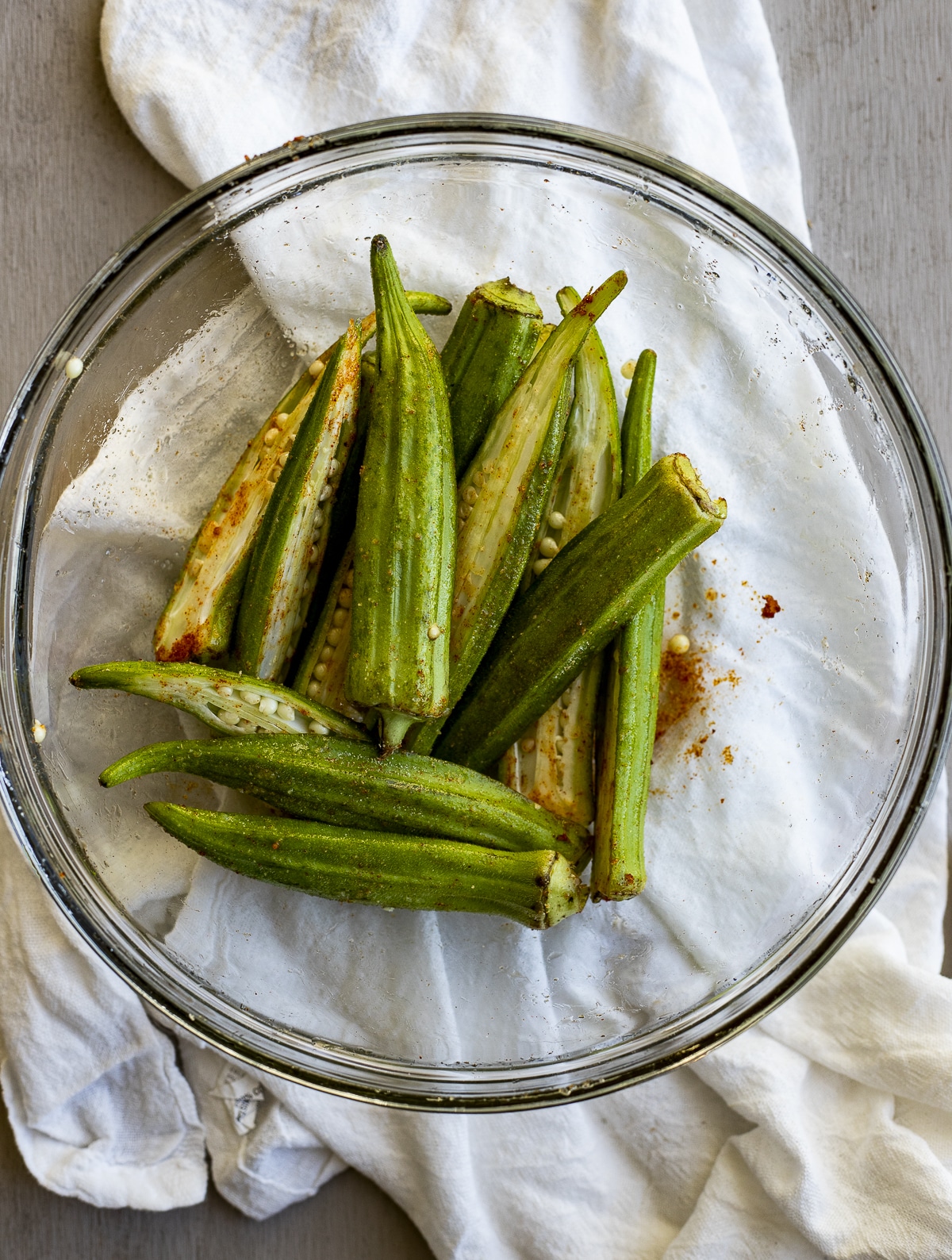 Sliced okra in a glass bowl and tossed with oil and seasonings.