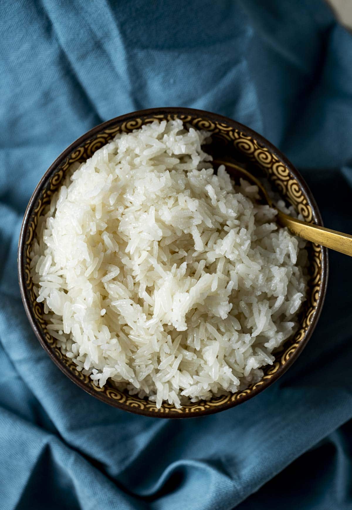 Overhead view of jasmine rice in a bowl with a spoon inserted into it.