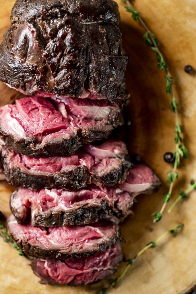 Overhead view of cooked and sliced venison loin on a wooden board.