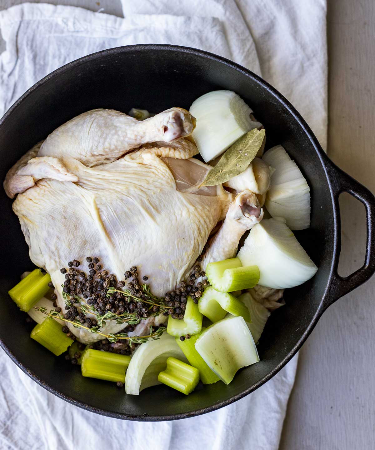 A whole raw chicken with veggies and seasonings in a large dutch oven to make broth.