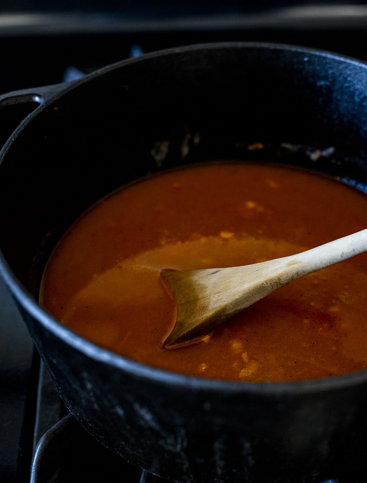 Liquid base of the bisque being stirred around in a Dutch oven with a wooden spoon.