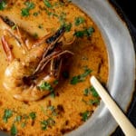 Prawn bisque in a grey bowl with a spoon inserted into it.