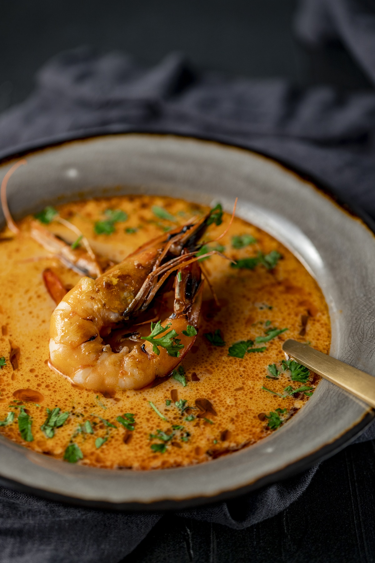 Side view of bisque in a grey bowl with a prawn on top.