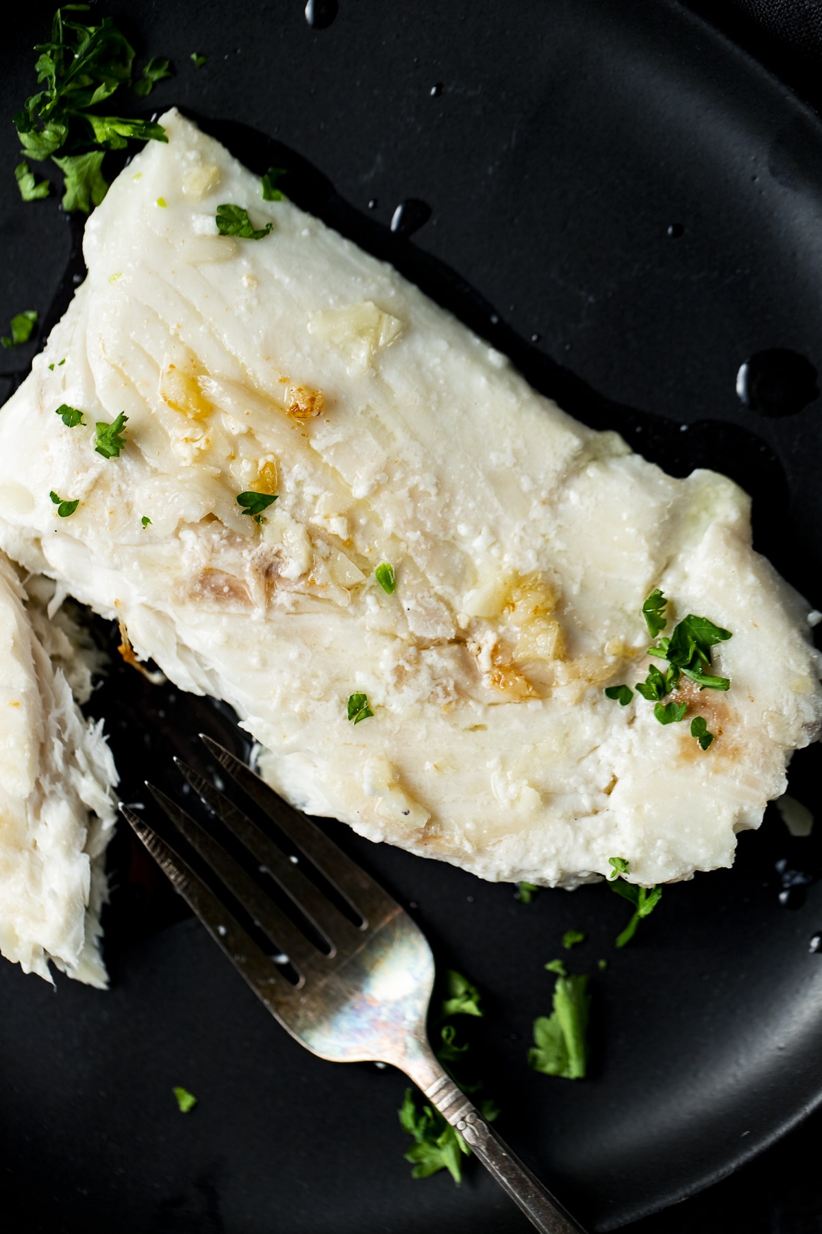 Overhead view of halibut on a black plate with a fork.