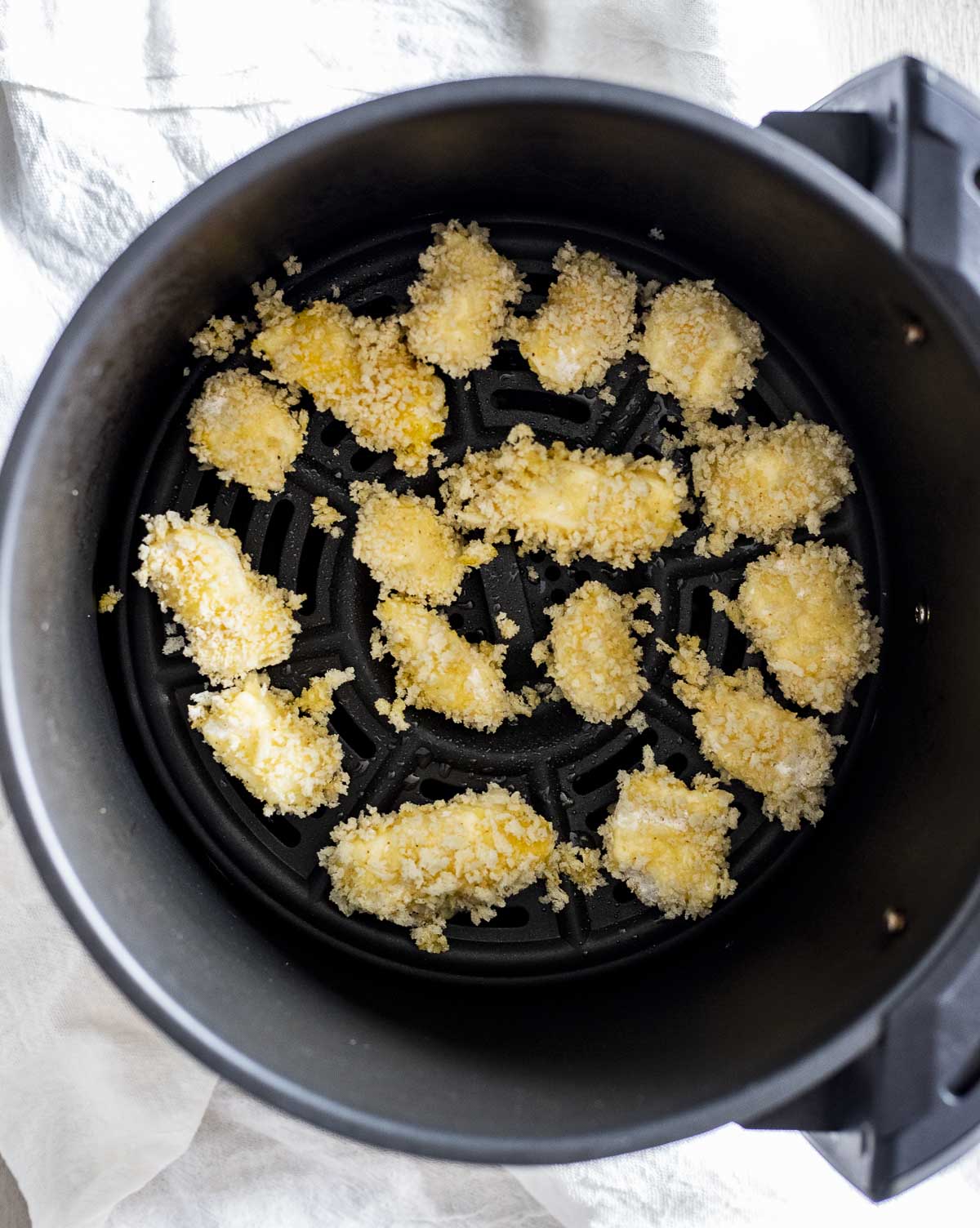 Overhead view of breaded cheese curds in an air fryer basket.