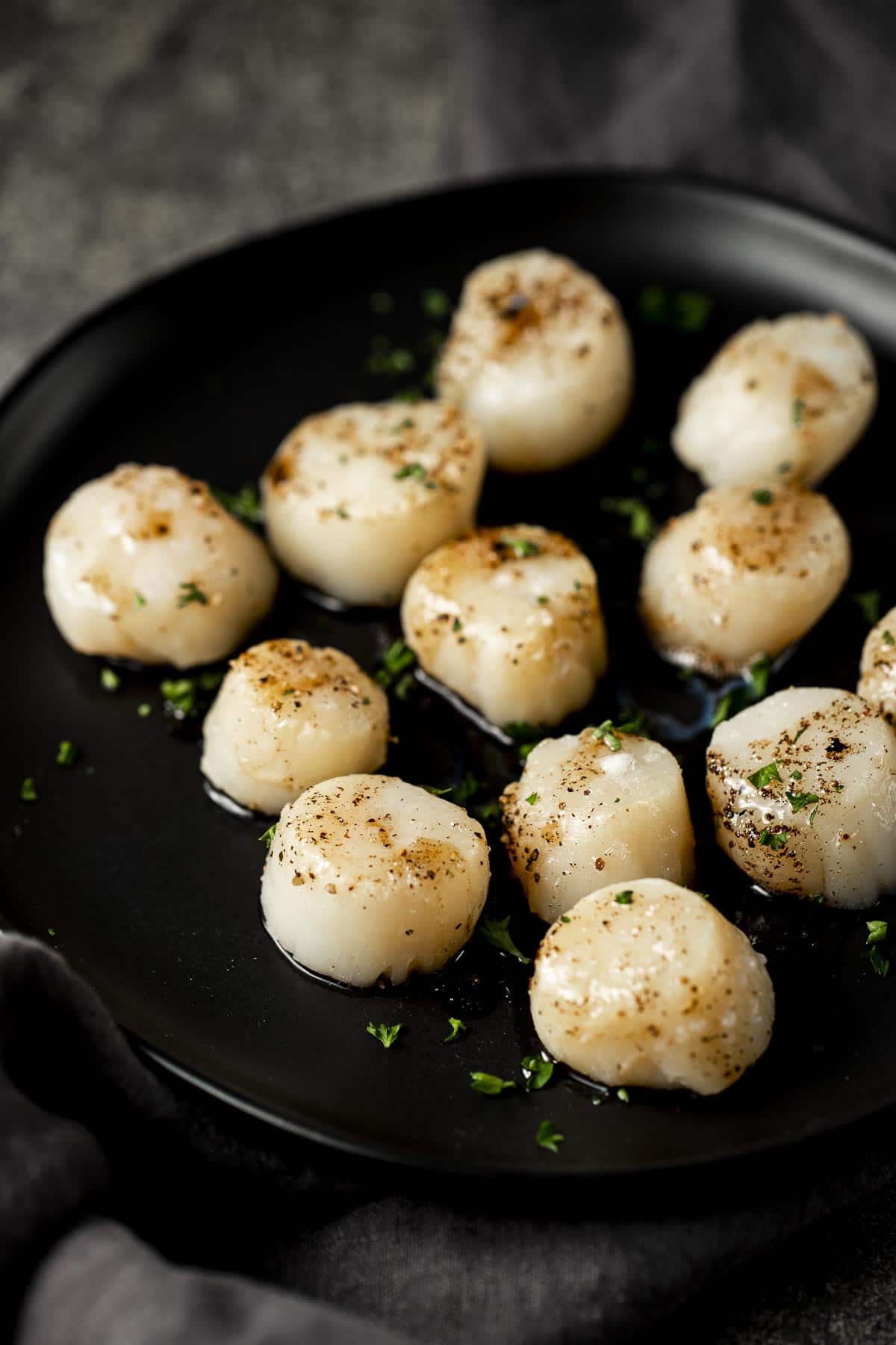 Broiled scallops with browned butter served on a black plate.