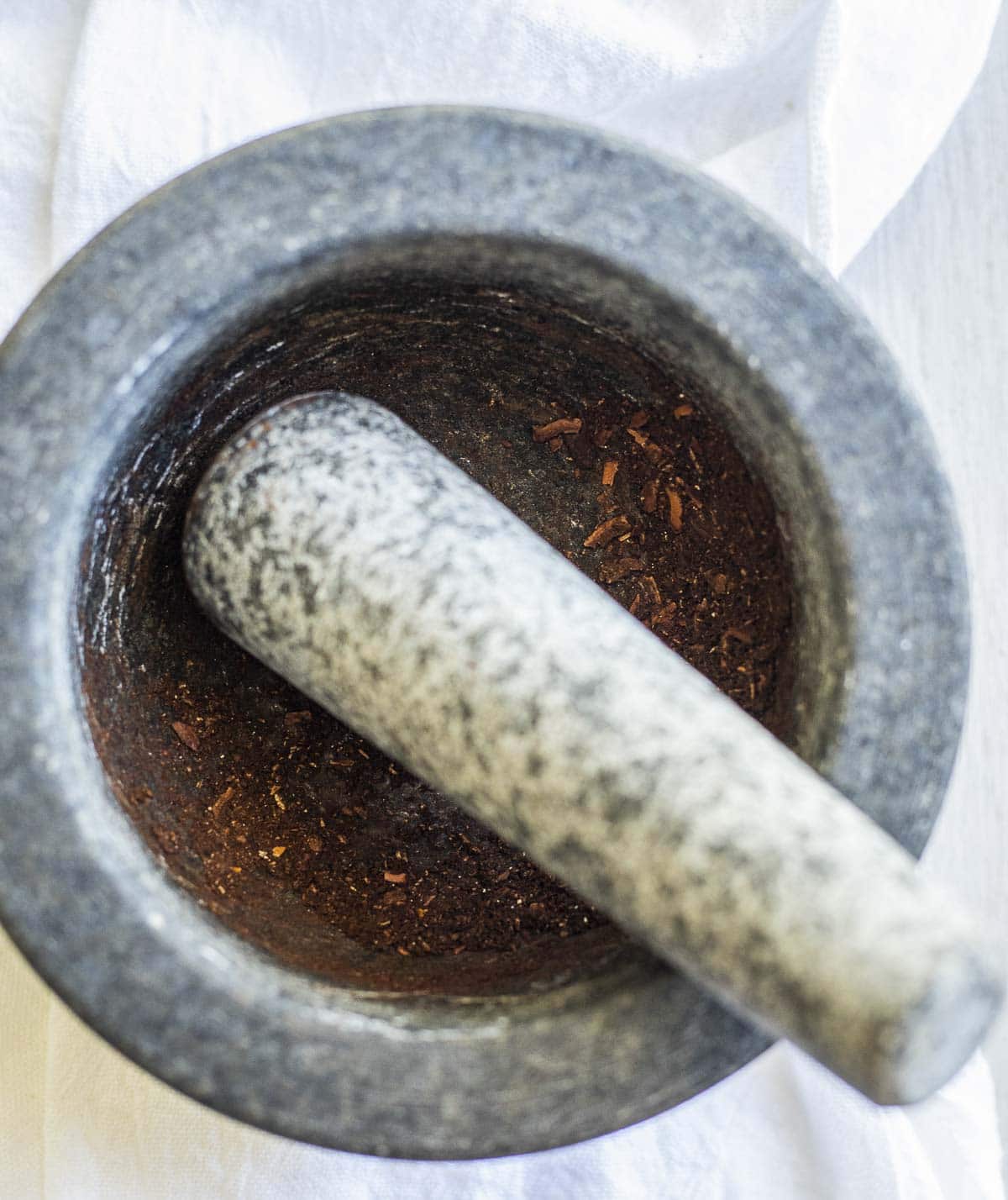 Toasted spices being ground together using a pestle and mortar.