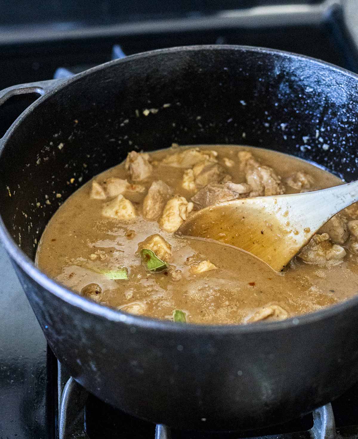 Chicken rendang cooking down in a large pot and being stirred with a wooden spoon.