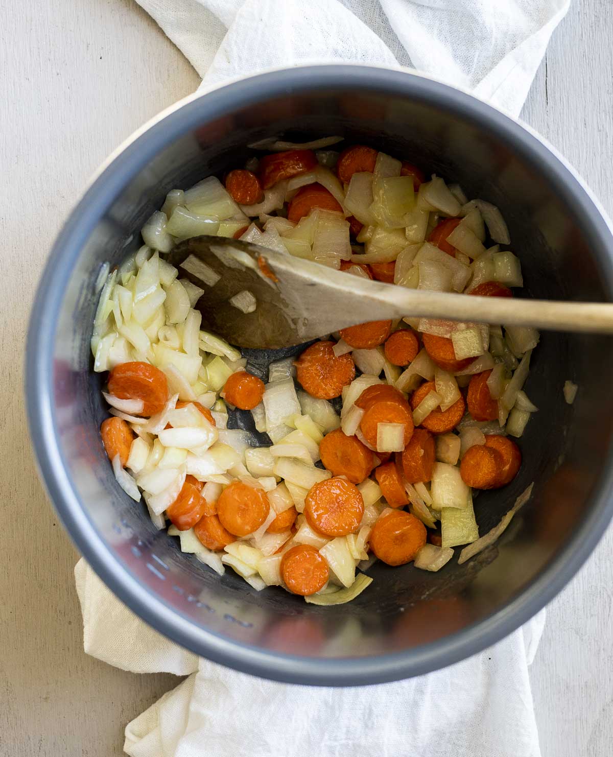 Chopped veggies for the pot pie in an Instant Pot insert with a wooden spoon.