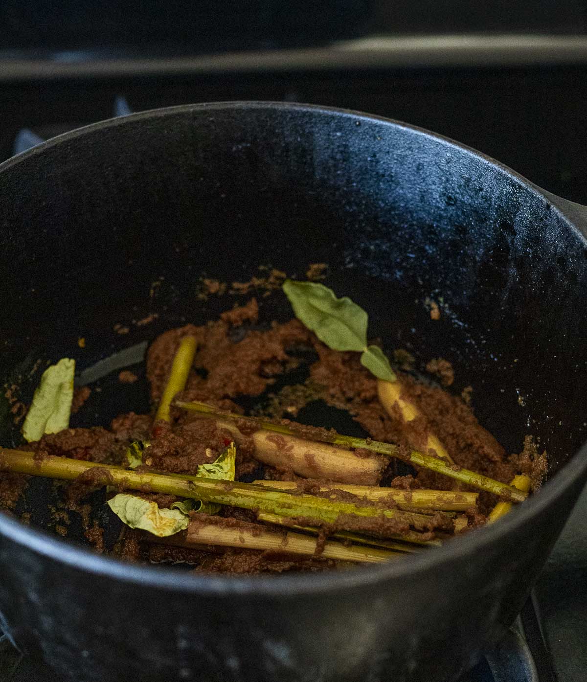 Laksa paste, kaffir lime leaves, lemongrass and Thai chilis being cooked in a large pot.