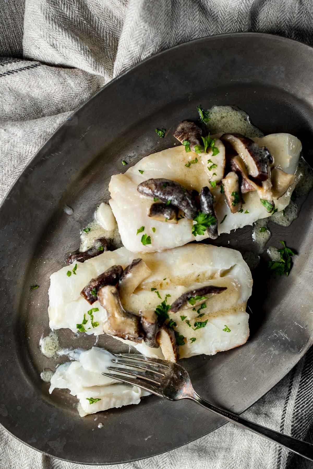 Two cod fillets served on a platter with mushroom sauce on top.