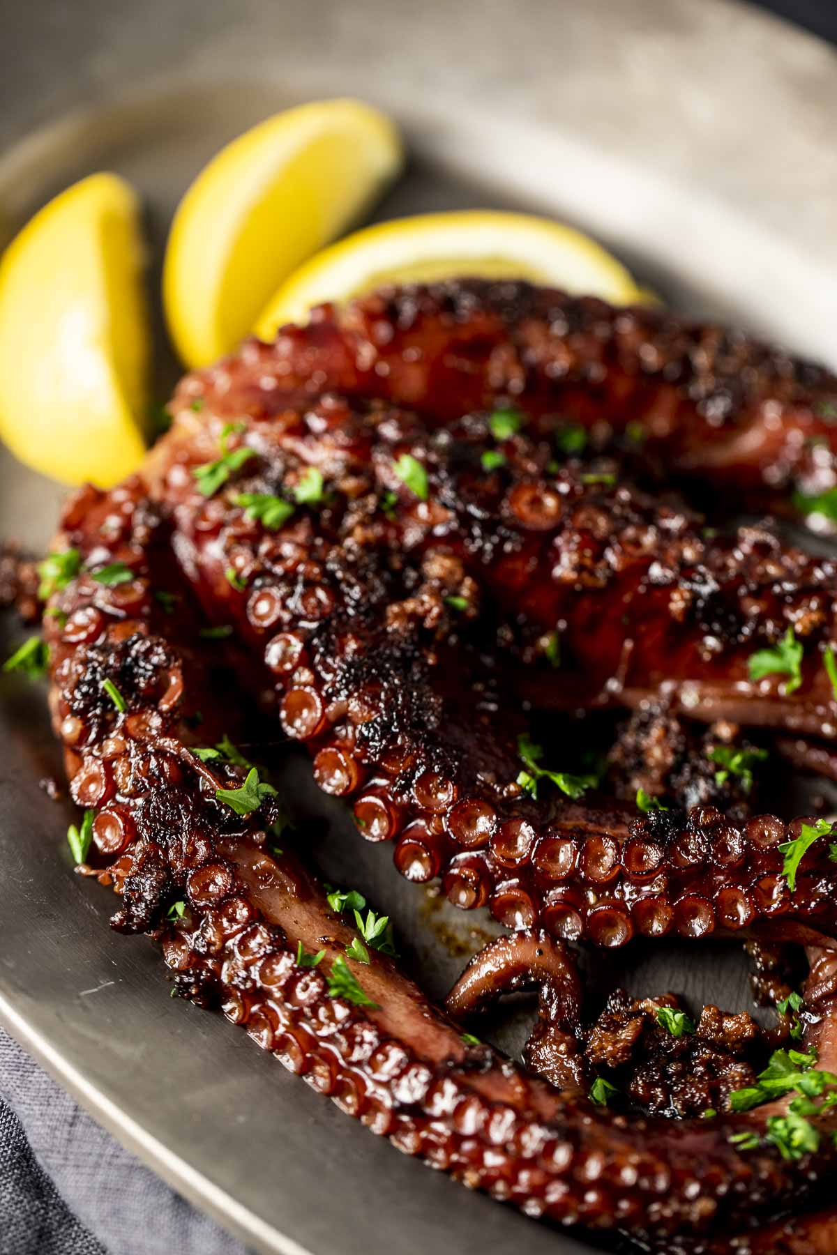 Side view of sous vide octopus on a plate and topped with chopped herbs.