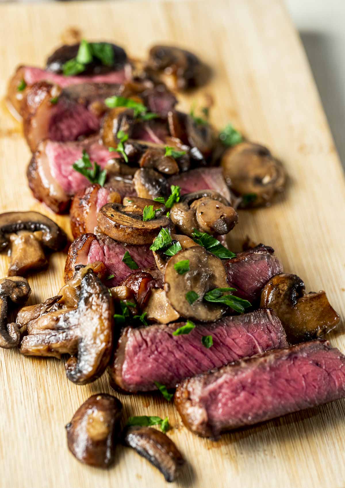 Sliced sous vide sirloin steak on a wooden board with sherry mushroom sauce on top.