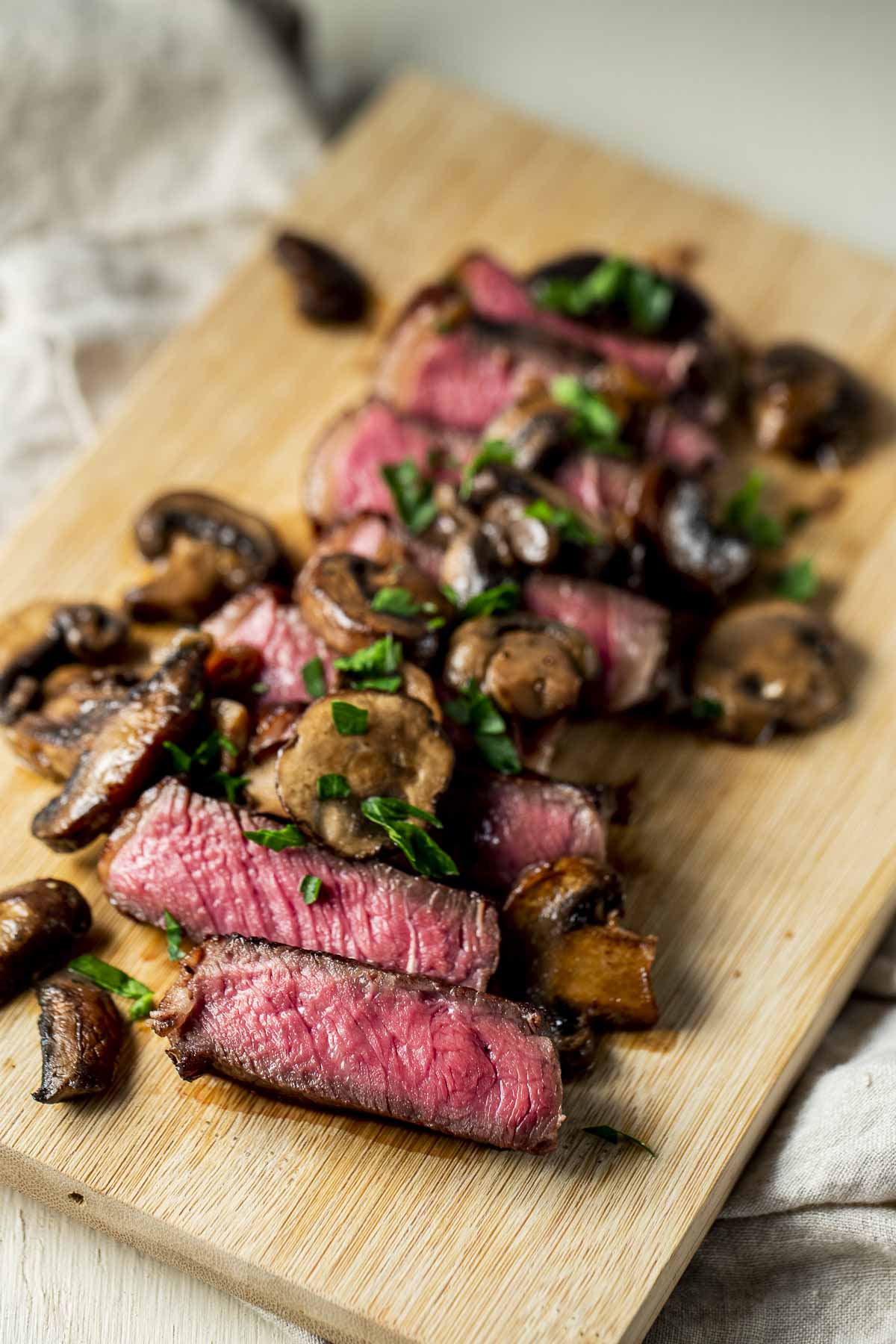 Sirloin steak cut into slices on a wooden board and topped with mushroom sauce.