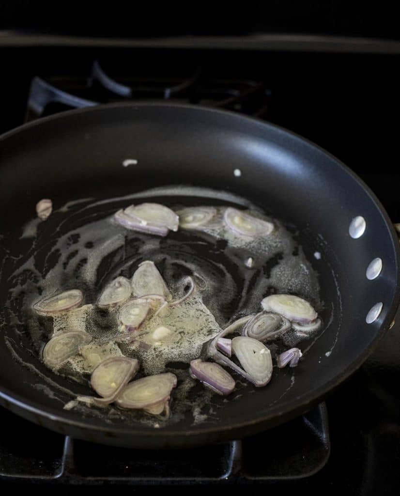 Sliced shallots being sautéed in butter in a skillet.