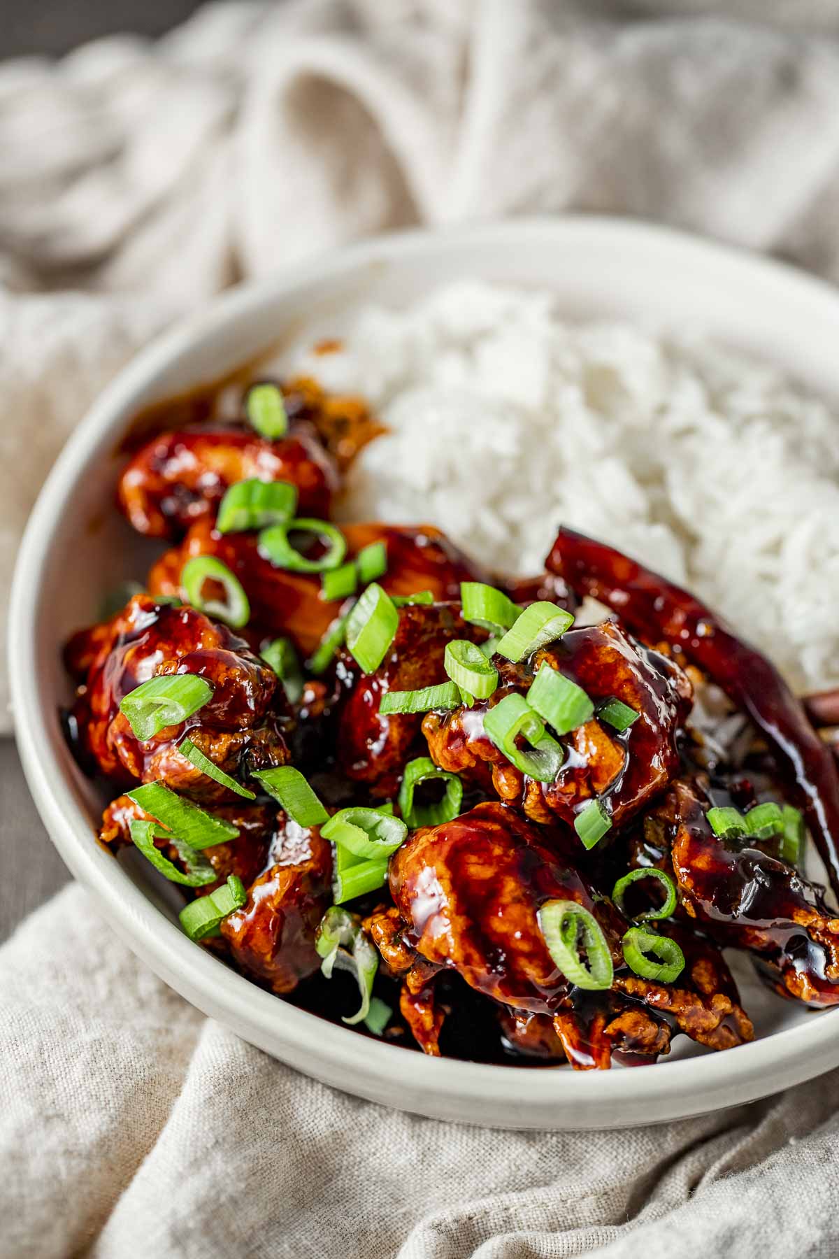 Side view of general tso's chicken with rice in a white bowl.
