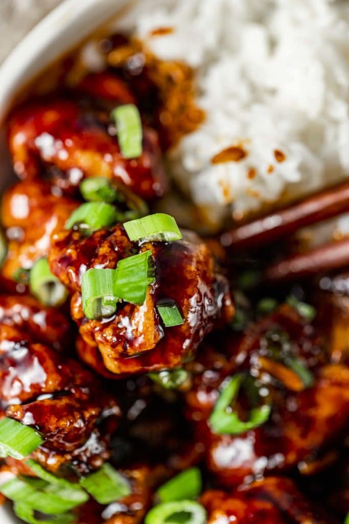 Close up of a piece of general tso's chicken topped with chopped green onion.