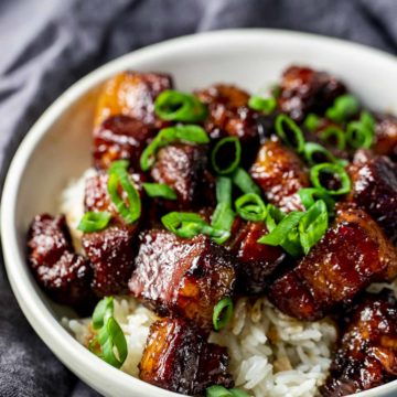 Chinese braised pork belly in a white bowl with rice and topped with chopped green onions.