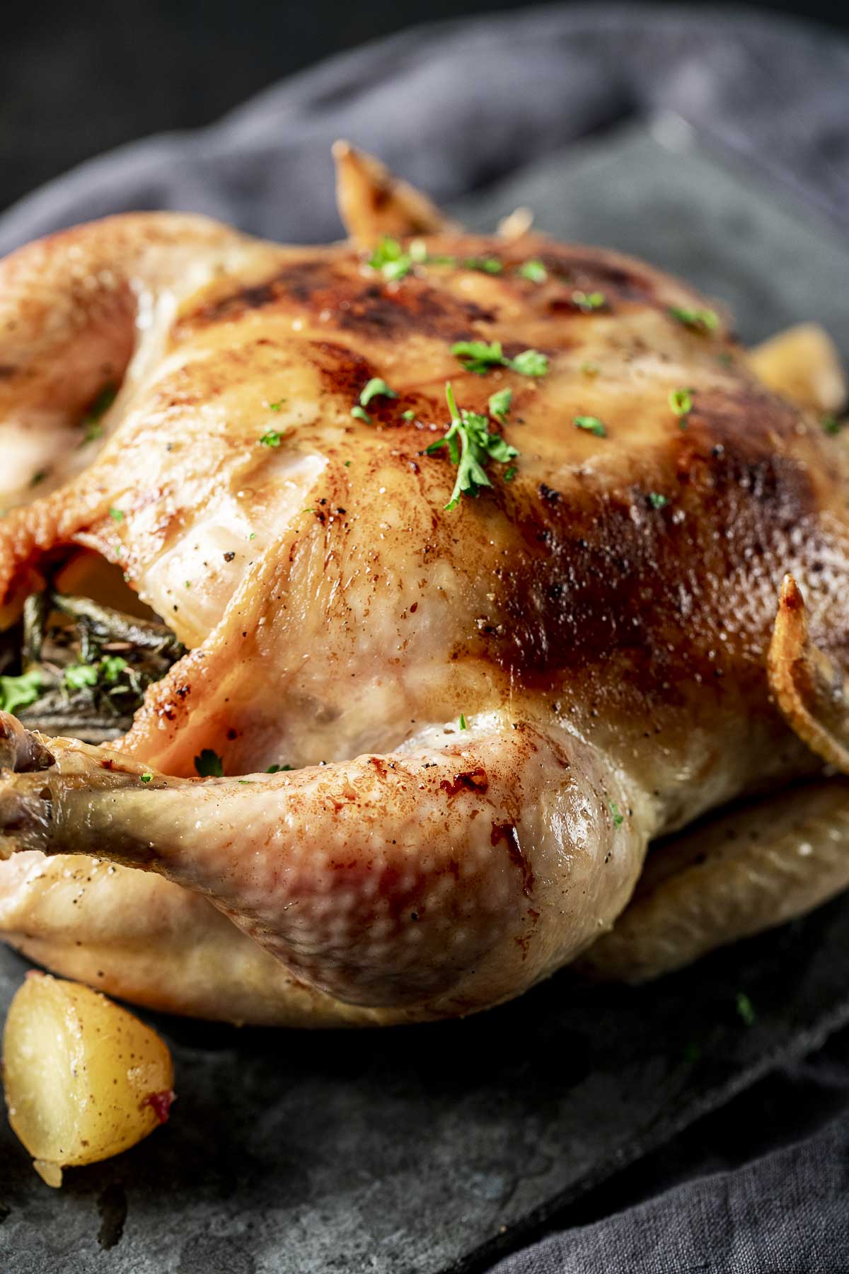 Side view of a whole roasted chicken with chopped fresh herbs on top.