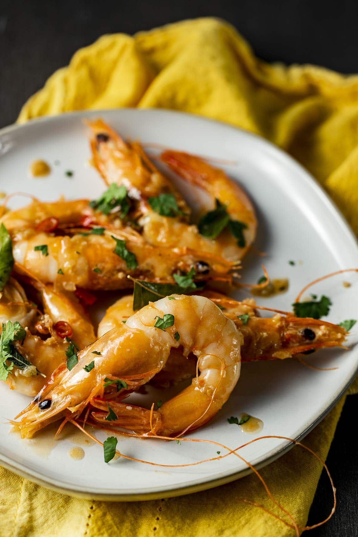 Butter prawns on a white plate on top of a yellow napkin.