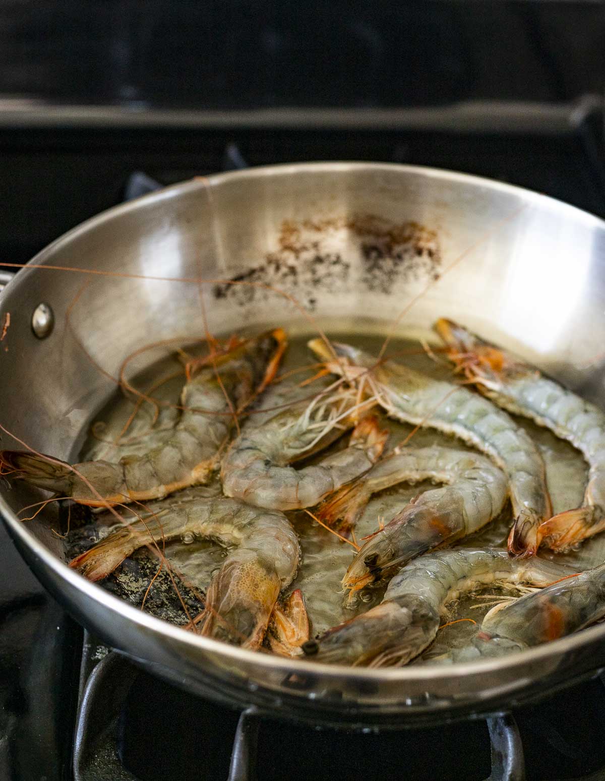 Prawns cooking in oil in a skillet on the stovetop.