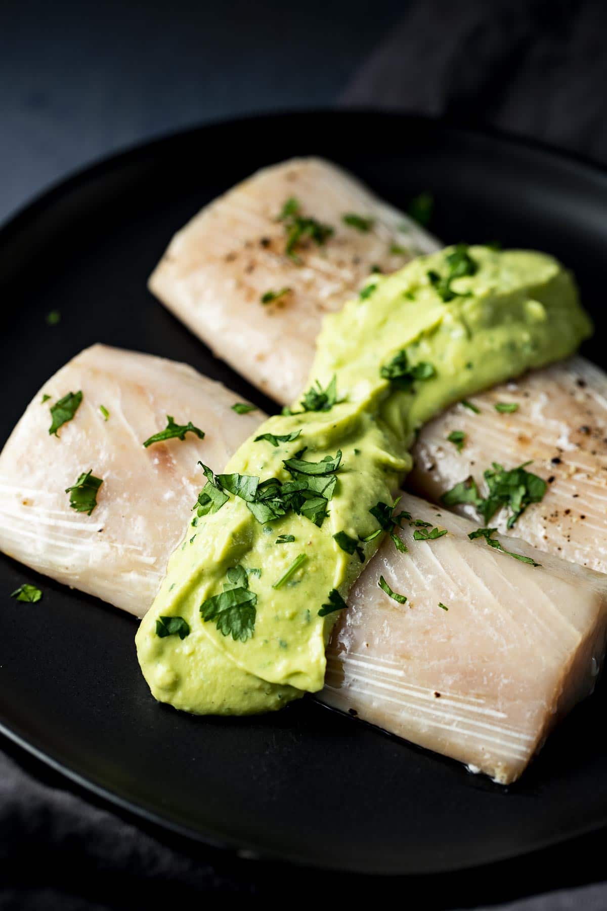 Side view of sous vide mahi mahi on a black plate and topped with avocado cilantro cream sauce.