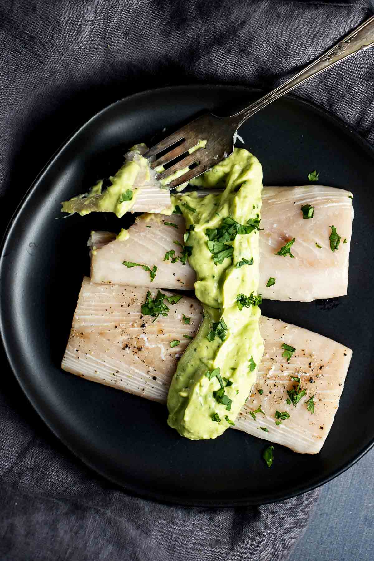 Overhead view of two fillets of mahi mahi on a black plate and topped with avocado cilantro cream sauce.